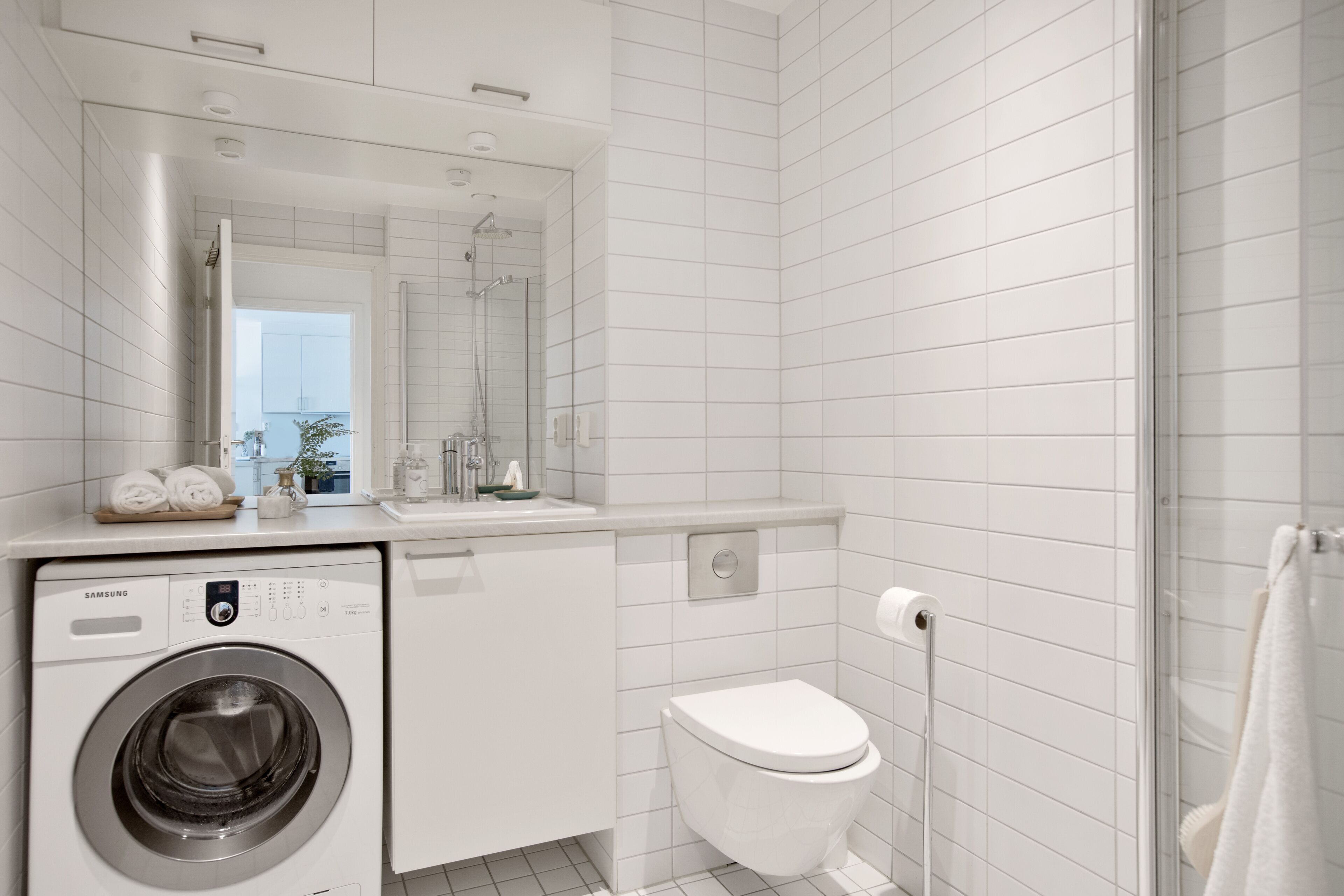 Ein modernes Badezimmer mit Waschmaschine, Toilette und Duschkabine aus Glas.