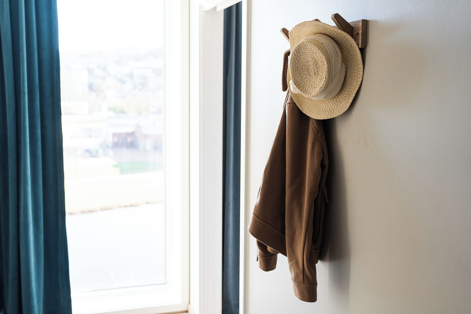 Une pièce avec une fenêtre, un chapeau accroché au mur et une veste suspendue.