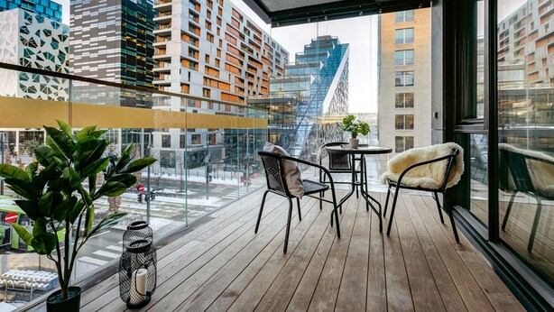 Un balcon doté d’un plancher en bois, de chaises en métal noir, d’une petite table ronde et d’une plante en pot.