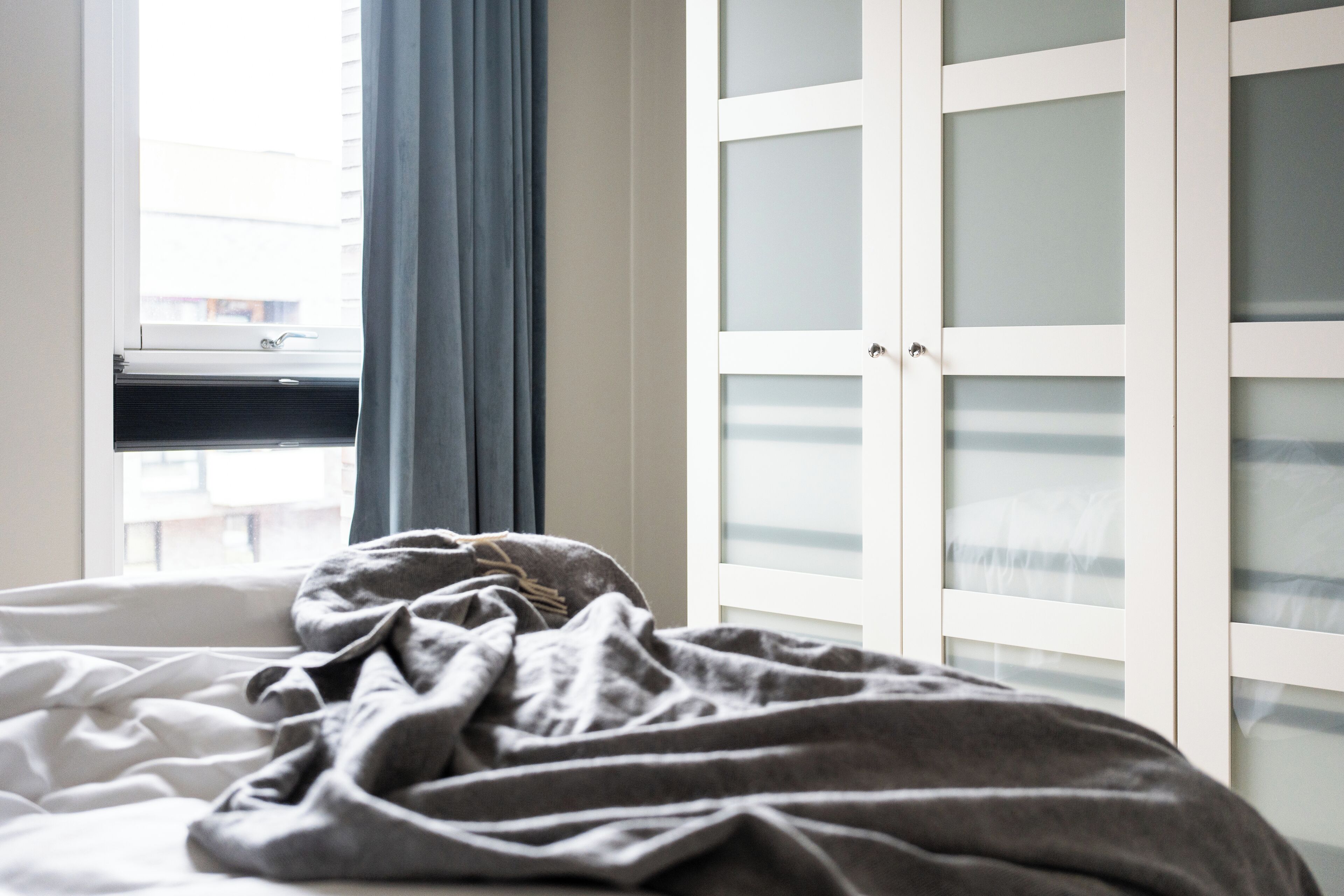 A bedroom with a bed, a window with blinds, and a wardrobe with frosted glass doors.