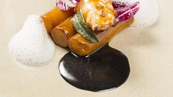 A dessert plate with a caramelized fruit arrangement, garnished with a green leaf and purple flowers, on a beige ceramic plate.