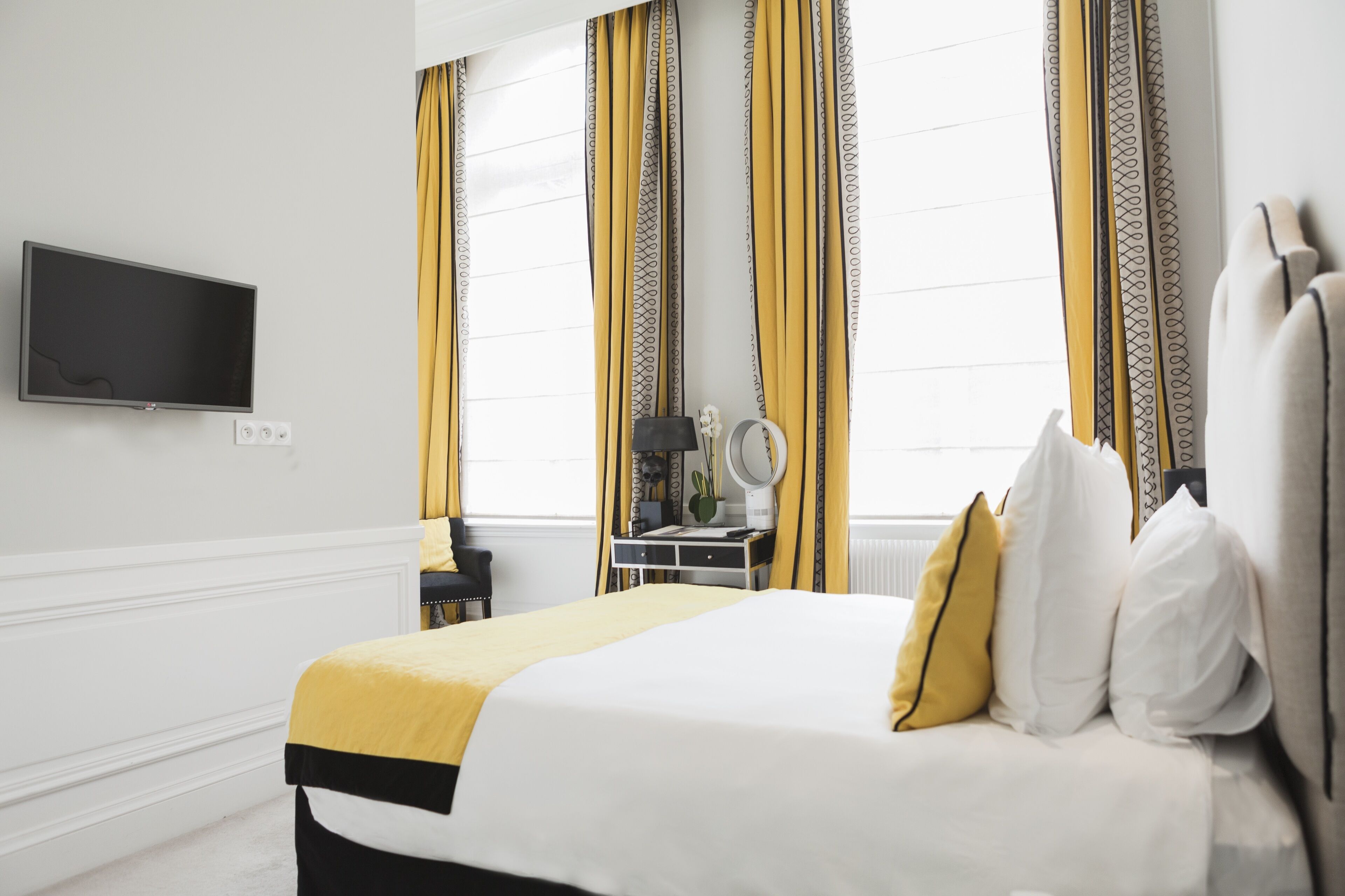 A neatly arranged hotel room with a bed, a bedside table, a mirror, and a TV mounted on the wall.
