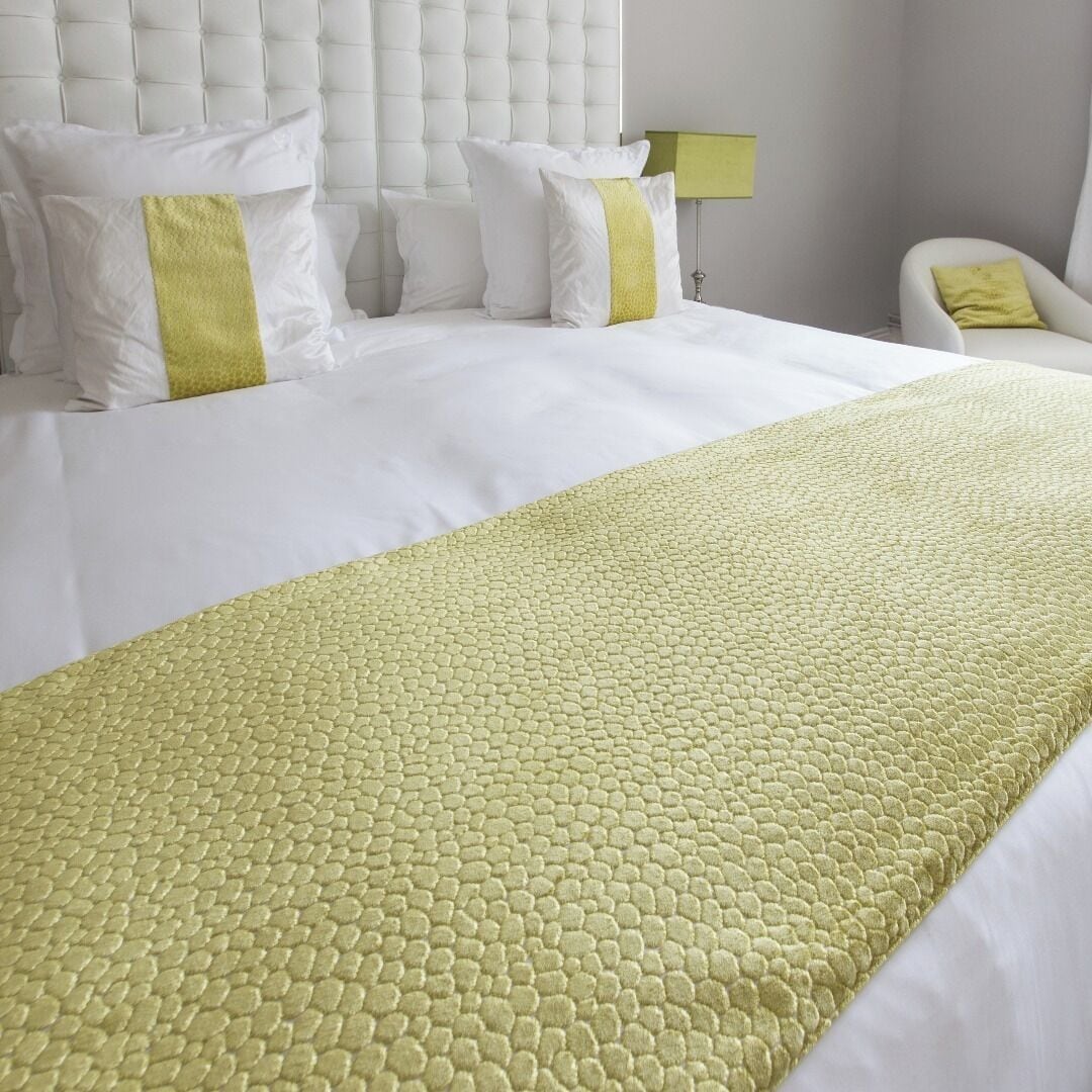 A hotel room with a large bed, a tufted headboard, and a green accent pillow.