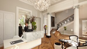 A reception area with a marble counter, a chandelier, a staircase, and a seating area with a magazine. - Clarance Hotel Lille (Lille)