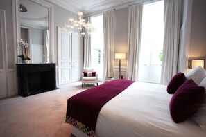 A spacious bedroom with a large bed, a fireplace, a chandelier, and a view of the outdoors. - Clarance Hotel Lille (Lille)