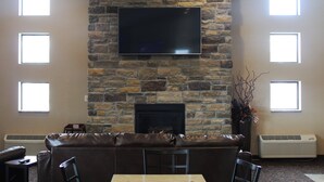 A stone fireplace with a flat-screen TV above it, a leather sofa, and a table with chairs. - Cobblestone Inn & Suites - Denison - Oak Ridge (Denison)