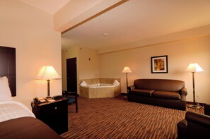 Hotelkamer met een bed, een slaapbank, een stoel, een bureau met lamp, een bureaulamp, een aan de muur hangend schilderij en een badkuip.