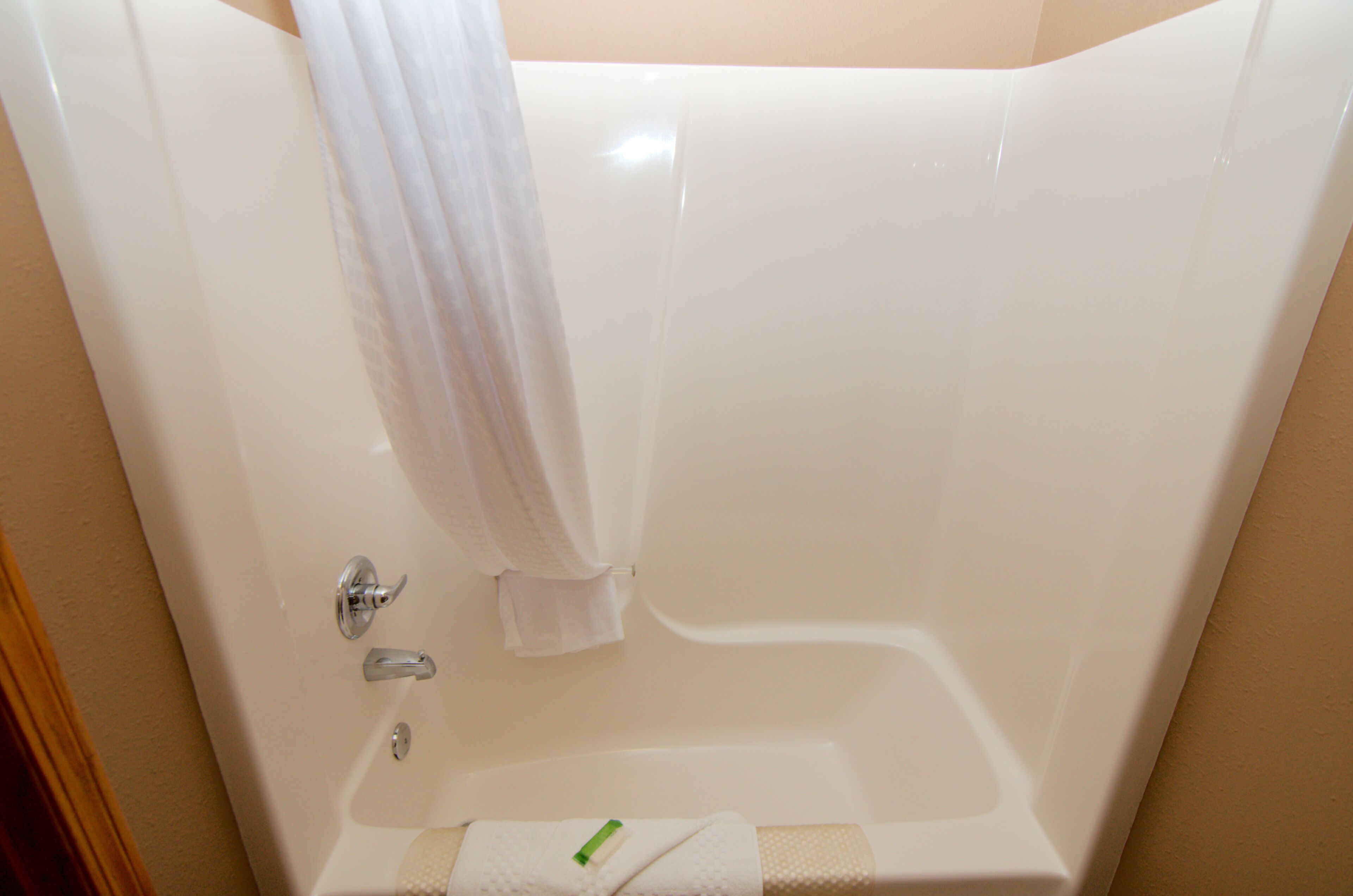Una bañera con cortina blanca, una toalla y un cepillo de dientes al lado.