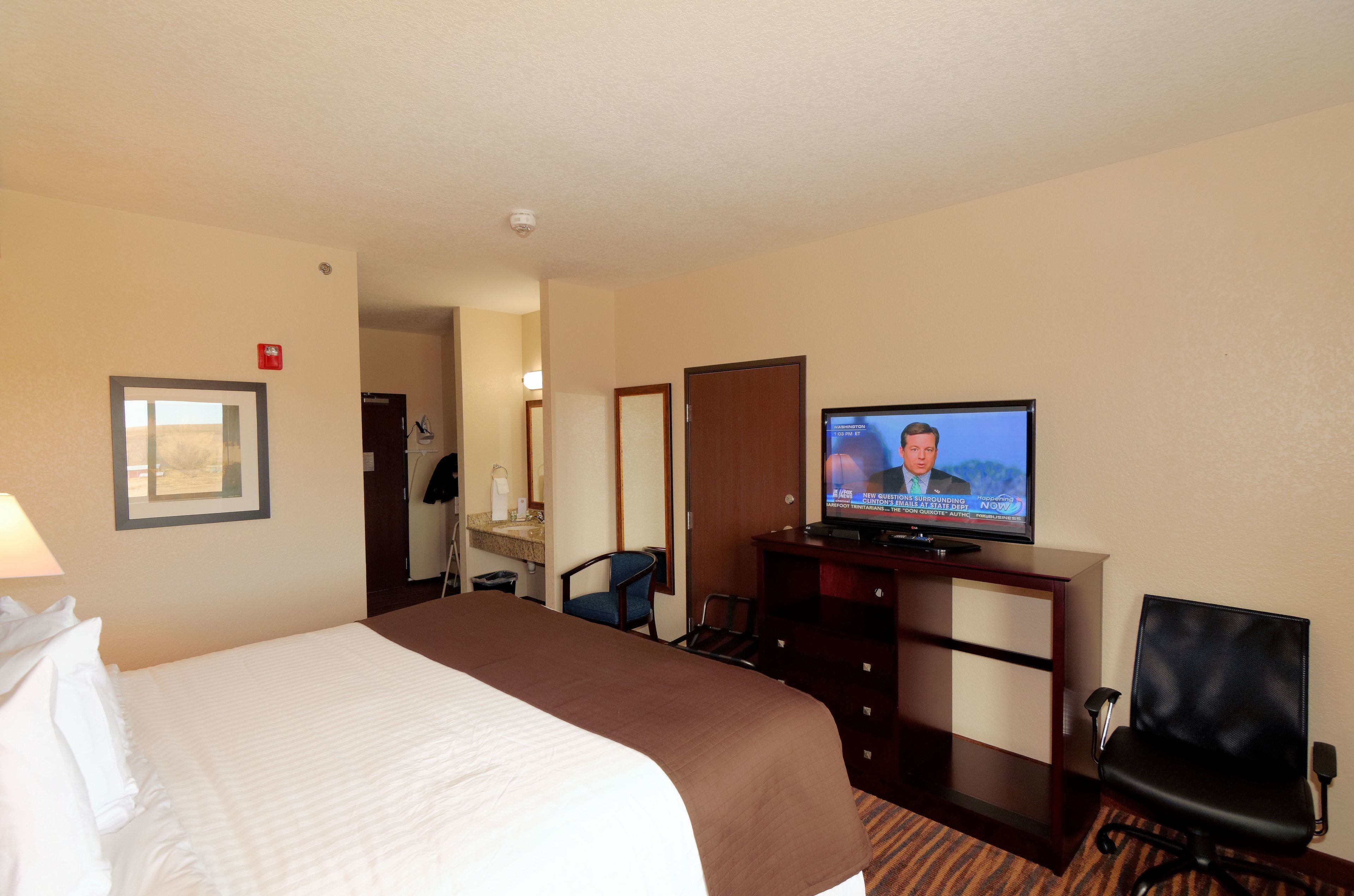 Une chambre d’hôtel avec un grand lit, une télévision, un bureau avec une chaise et une lampe de bureau.
