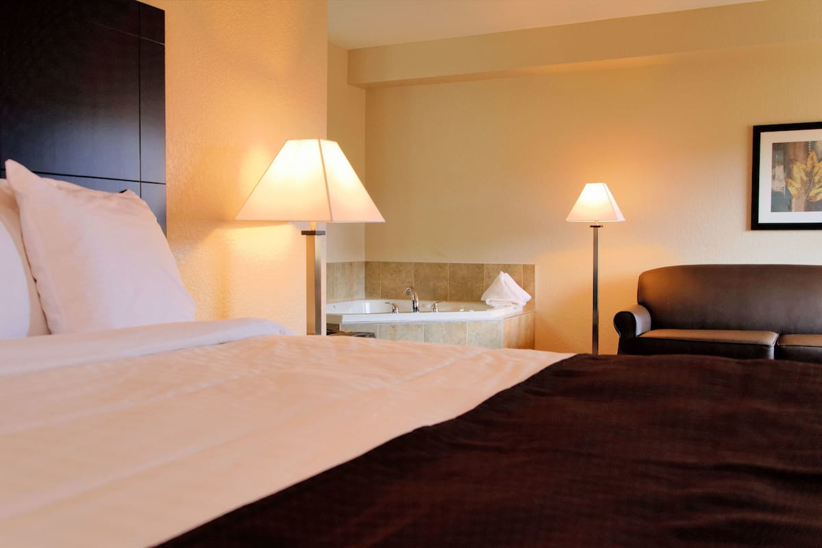 Une chambre d’hôtel comprenant un lit, deux lampes de chevet, une chaise et une salle de bain avec un lavabo et une baignoire.