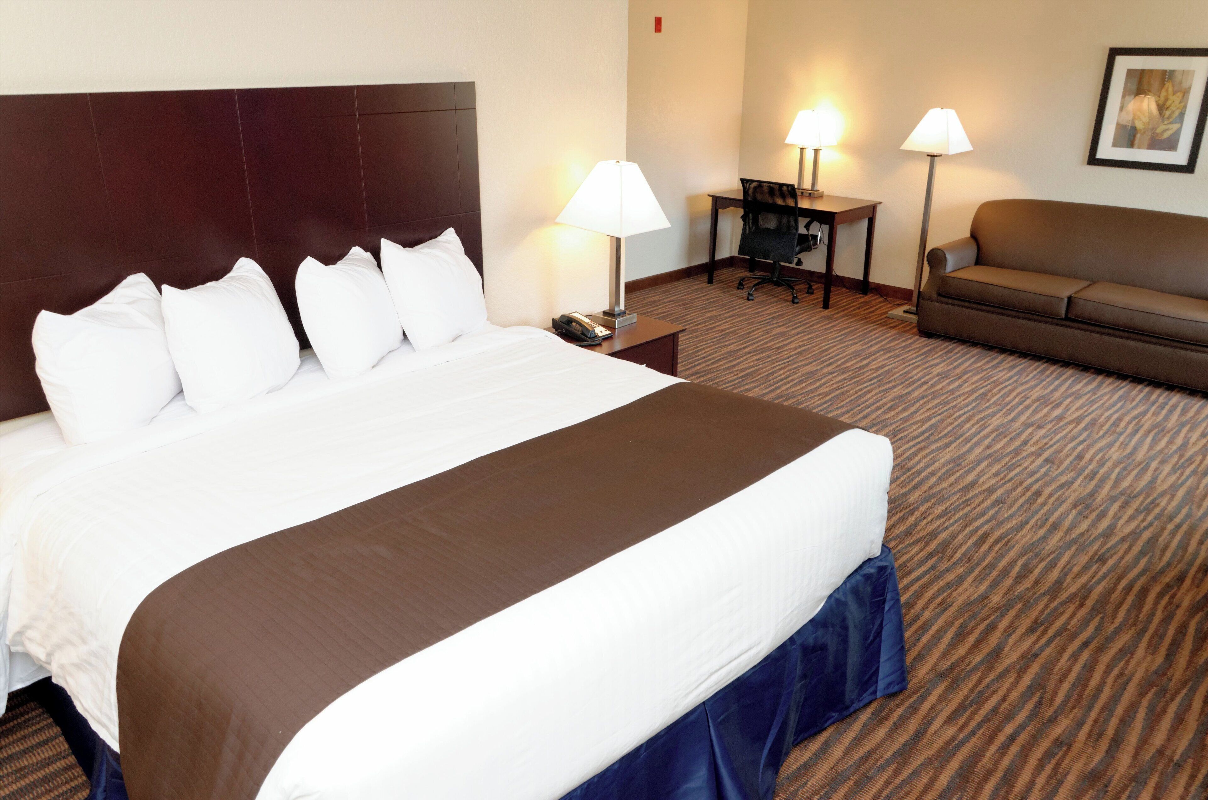 A hotel room with a large bed, a sofa, two lamps, and a desk.