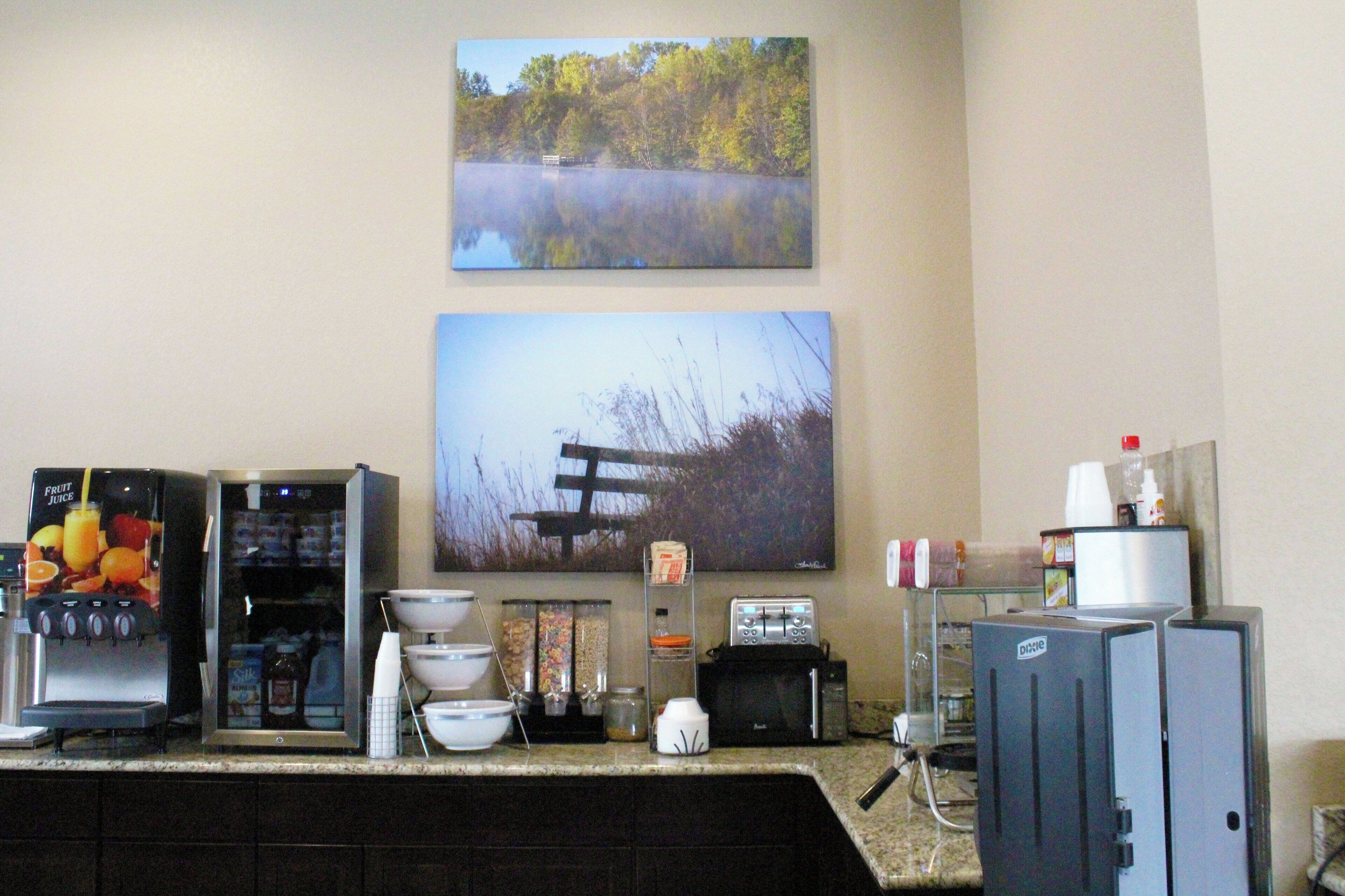 A kitchen area with a coffee machine, toaster, and a refrigerator. There are also various kitchen items and a painting of a landscape on the wall.