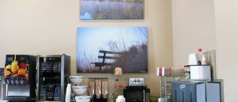 A kitchen area with a coffee machine, toaster, and a refrigerator. There are also various kitchen items and a painting of a landscape on the wall.