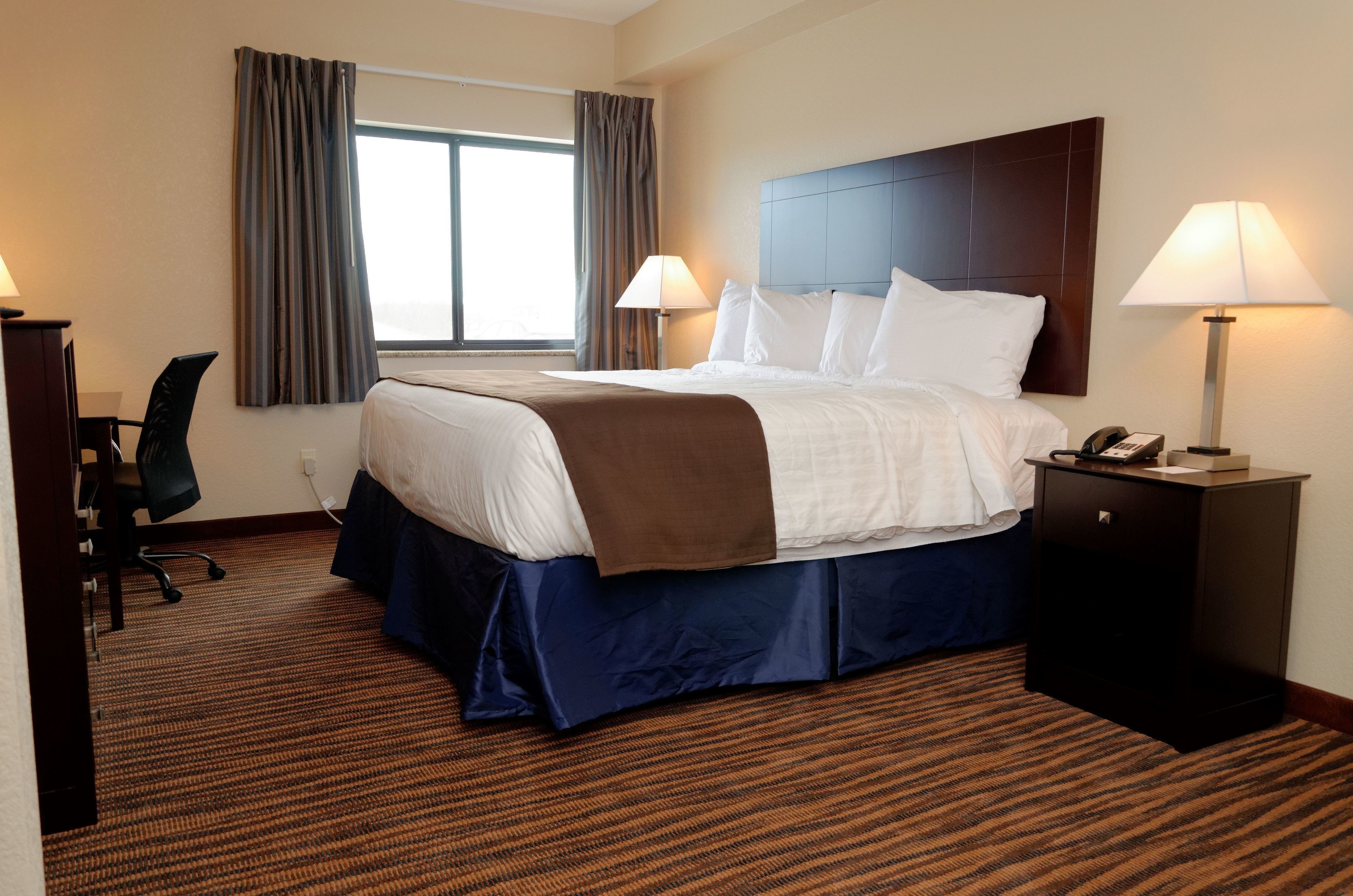 A hotel room with a large bed, two bedside lamps, a desk with a chair, and a window with curtains.