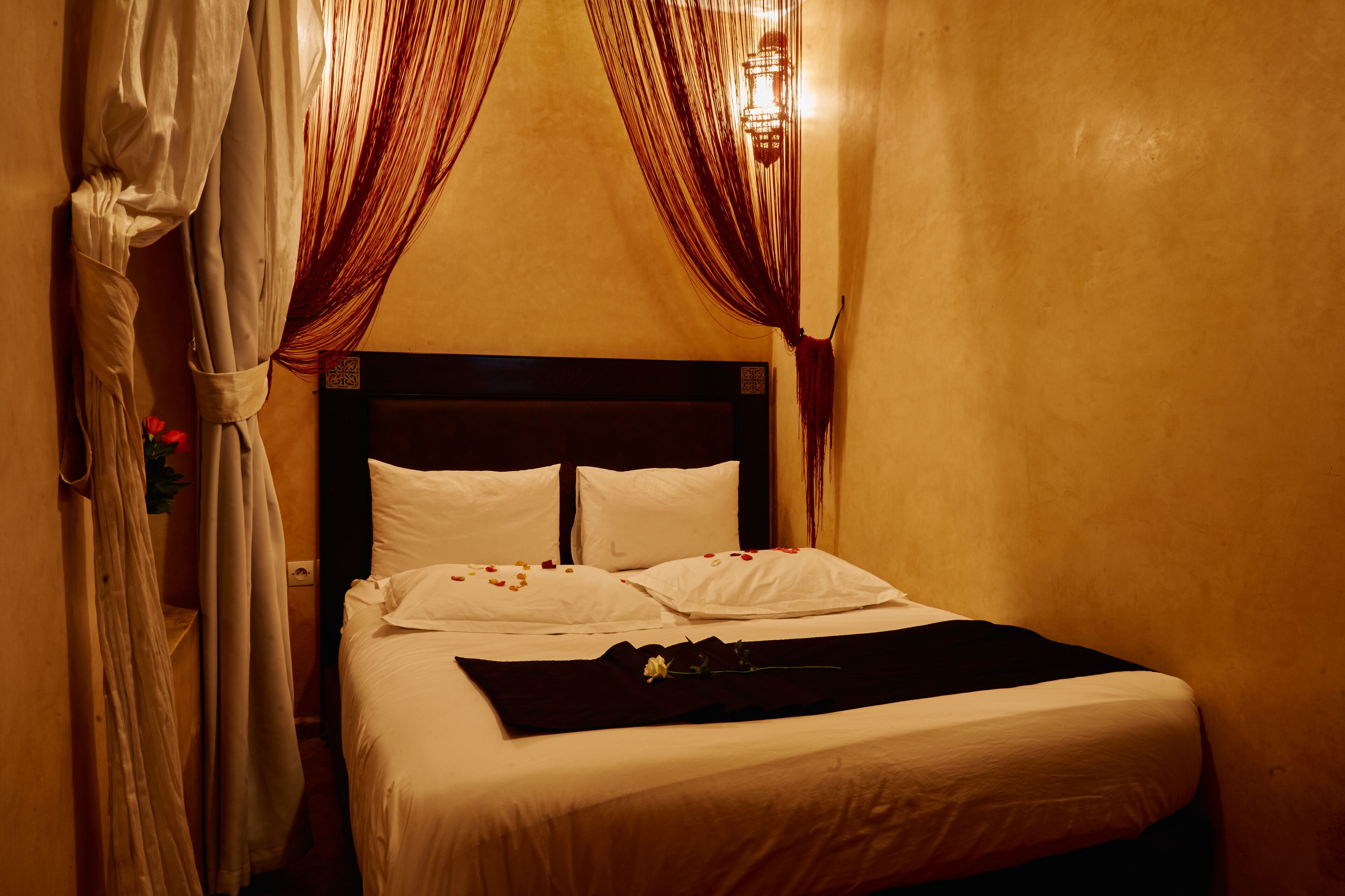 A neatly made bed with white linens, a dark headboard, and a decorative flower on the bedspread.