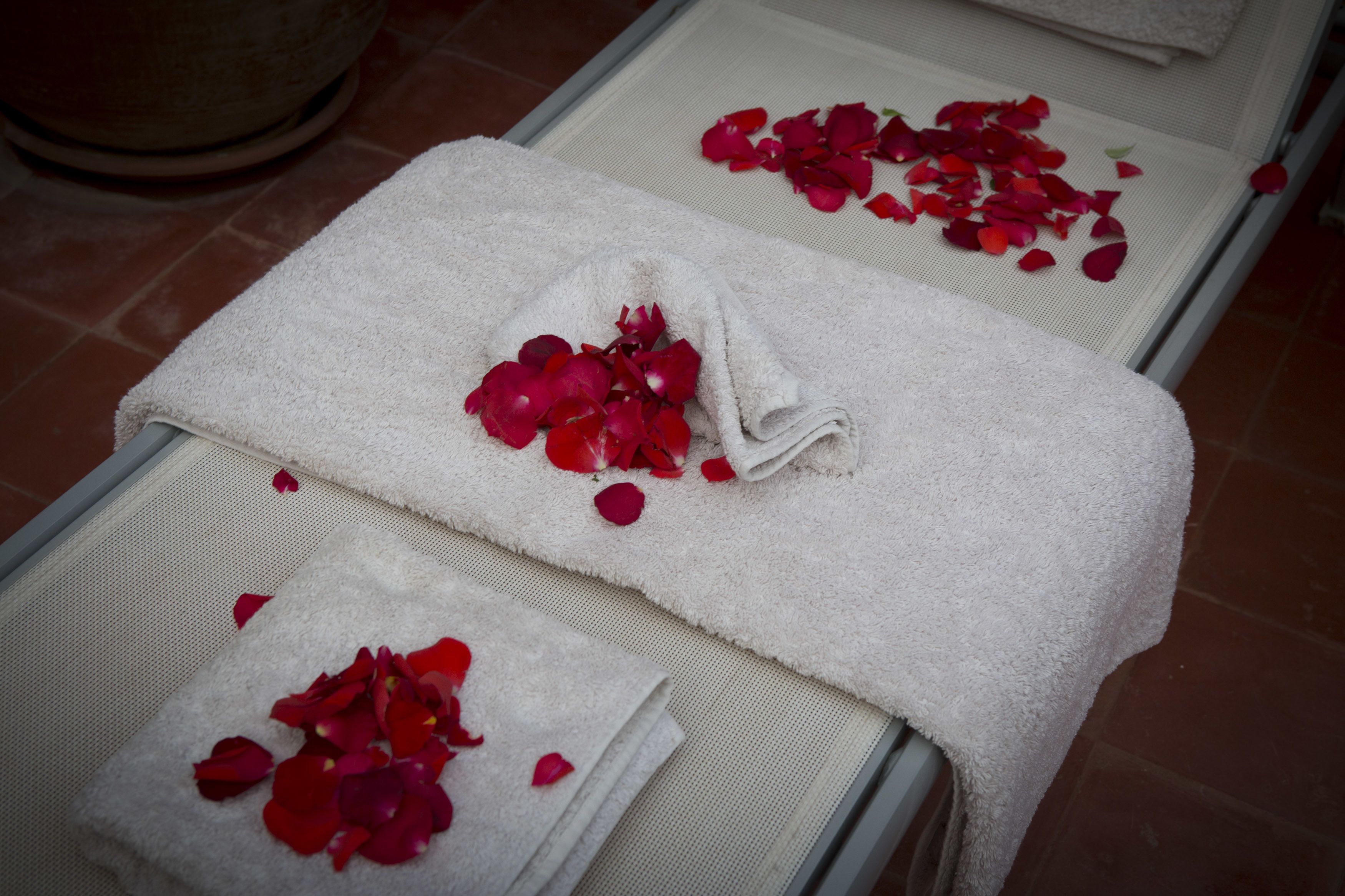 Un espace spa comprenant deux tables de massage recouvertes de serviettes blanches et de pétales de roses rouges.