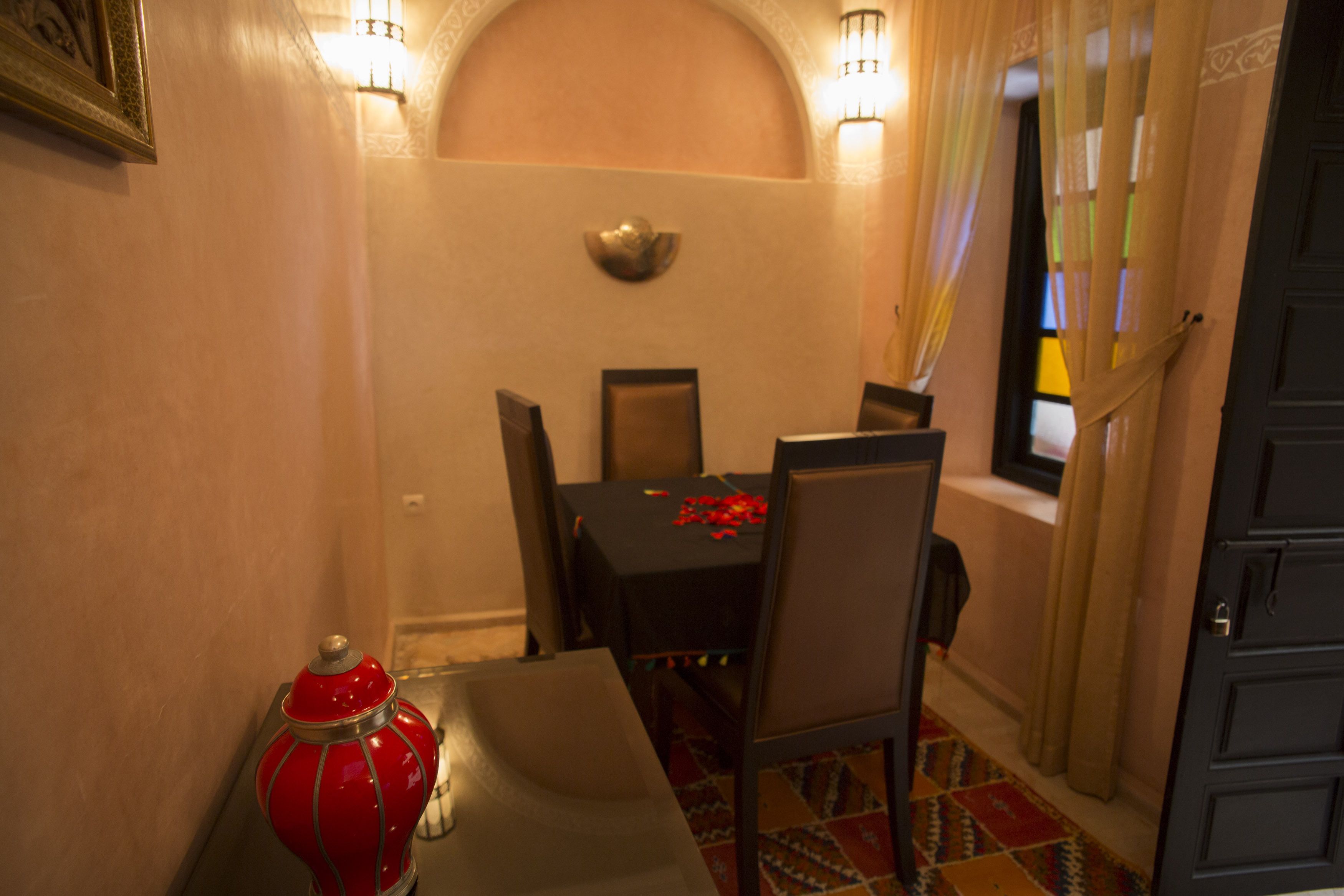 A dining area with a table set for two, a red decorative item on the table, and a window with curtains.