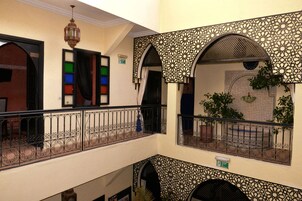 A multi-level interior with ornate metal railings, patterned walls, and a balcony with potted plants.