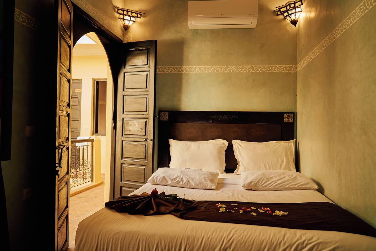A hotel room with a large bed, a wooden headboard, and a balcony visible through an open door.