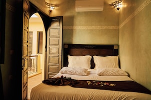 A hotel room with a large bed, a wooden headboard, and a balcony visible through an open door.