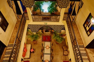 A spacious indoor area with a central seating area, a balcony with potted plants, and a patterned floor.