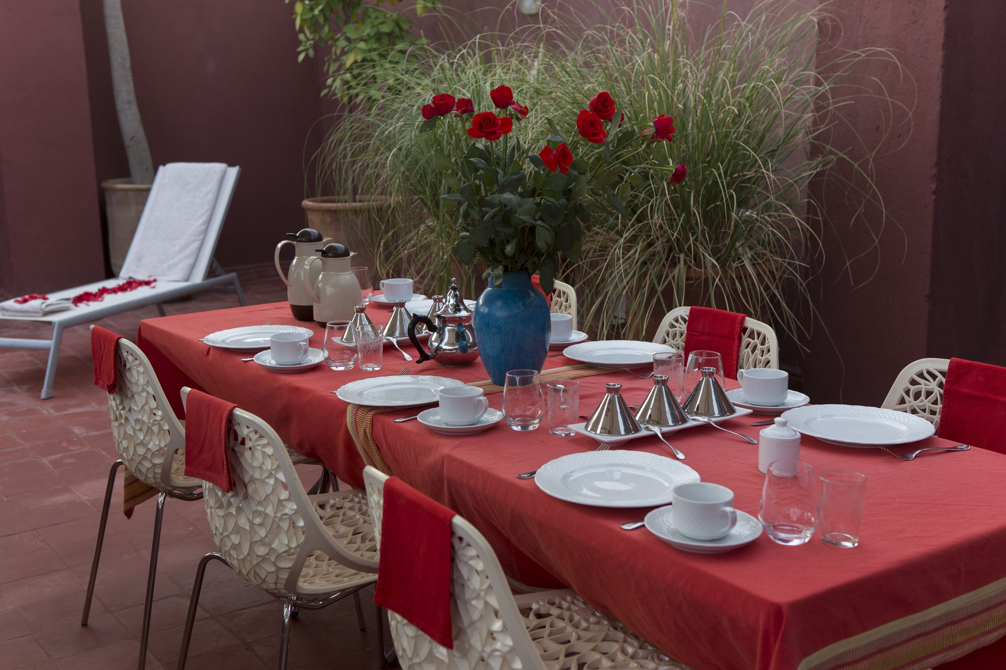 A table set for a meal with white plates, silverware, and a blue vase with red flowers.