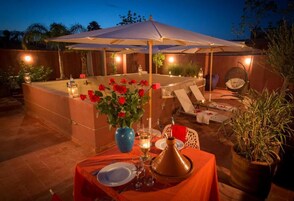 An outdoor dining area with a covered table, candles, and a decorative vase with red flowers.