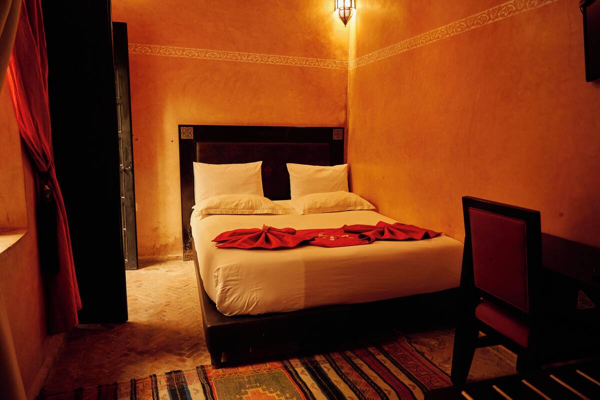 A hotel room with a bed, a chair, a patterned rug, and a wall with a decorative border.