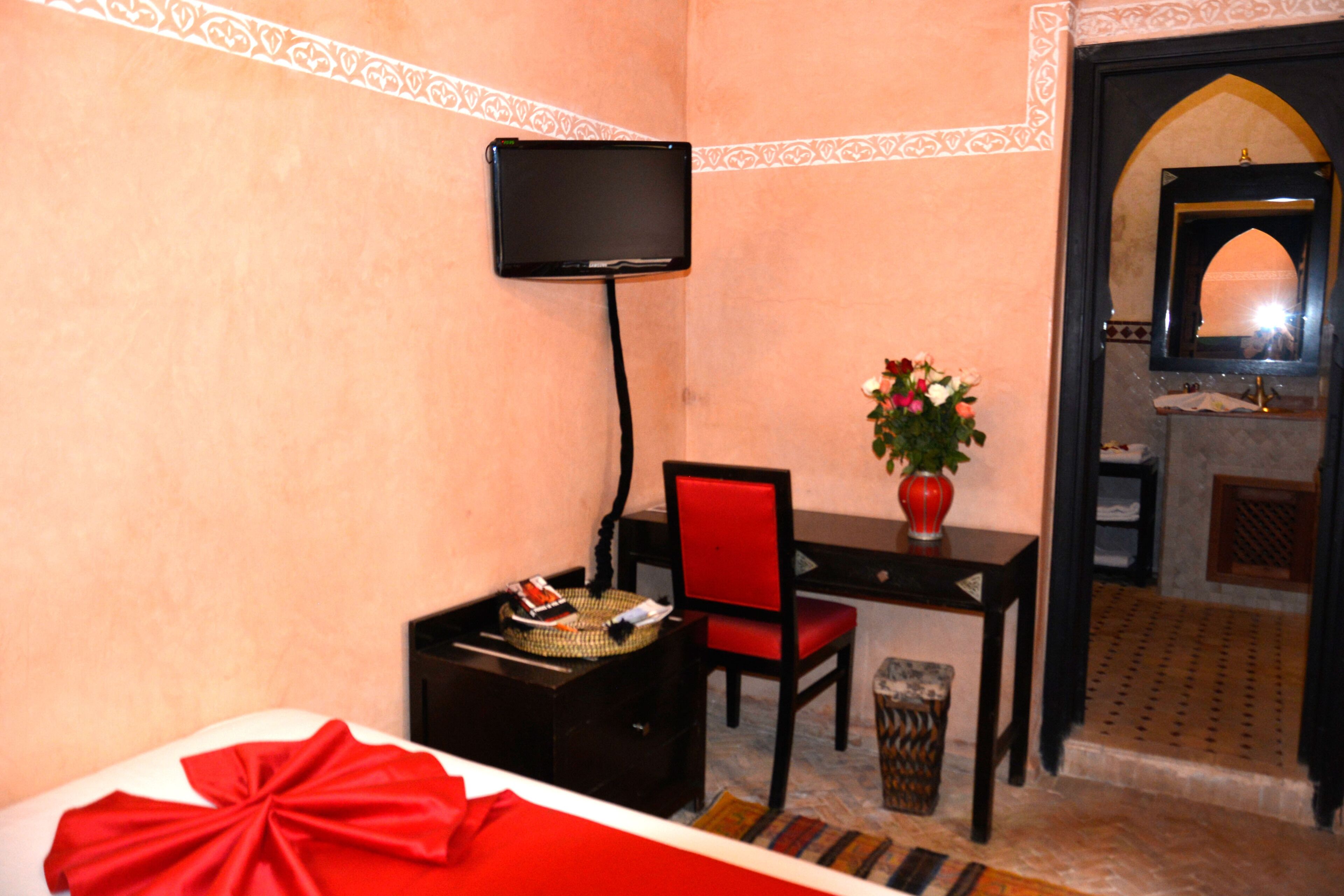 Habitació d'hotel amb llit, escriptori amb cadira, televisió penjada a la paret, ram de flors en un vas i mirall a la cantonada.