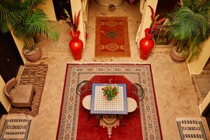 Una habitación con piso de baldosas, un tapete rojo, una mesa con sillas y plantas en macetas.