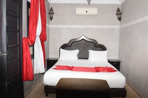 A hotel room with a large bed, two bedside tables, a red and white curtain, and a wall-mounted air conditioning unit.