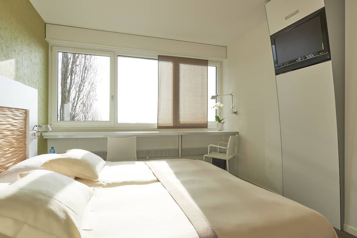 Ein Schlafzimmer mit einem großen Bett, einem Fenster mit Jalousien, einem Schreibtisch, einem Stuhl und einem Kleiderschrank.