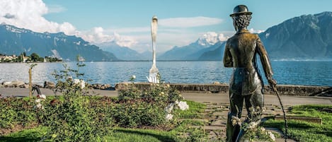 Una estatua de un hombre con un bastón en un parque con un lago y montañas al fondo.