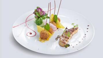 Ein weißer Teller mit verschiedenen Speisen, darunter gegrillter Fisch, eine Teigkugel und etwas Grünzeug.