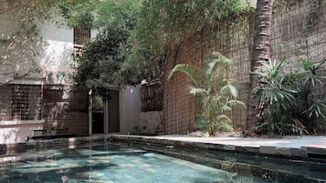 Una piscina de agua cristalina, rodeada por una valla de bambú y protegida por árboles.