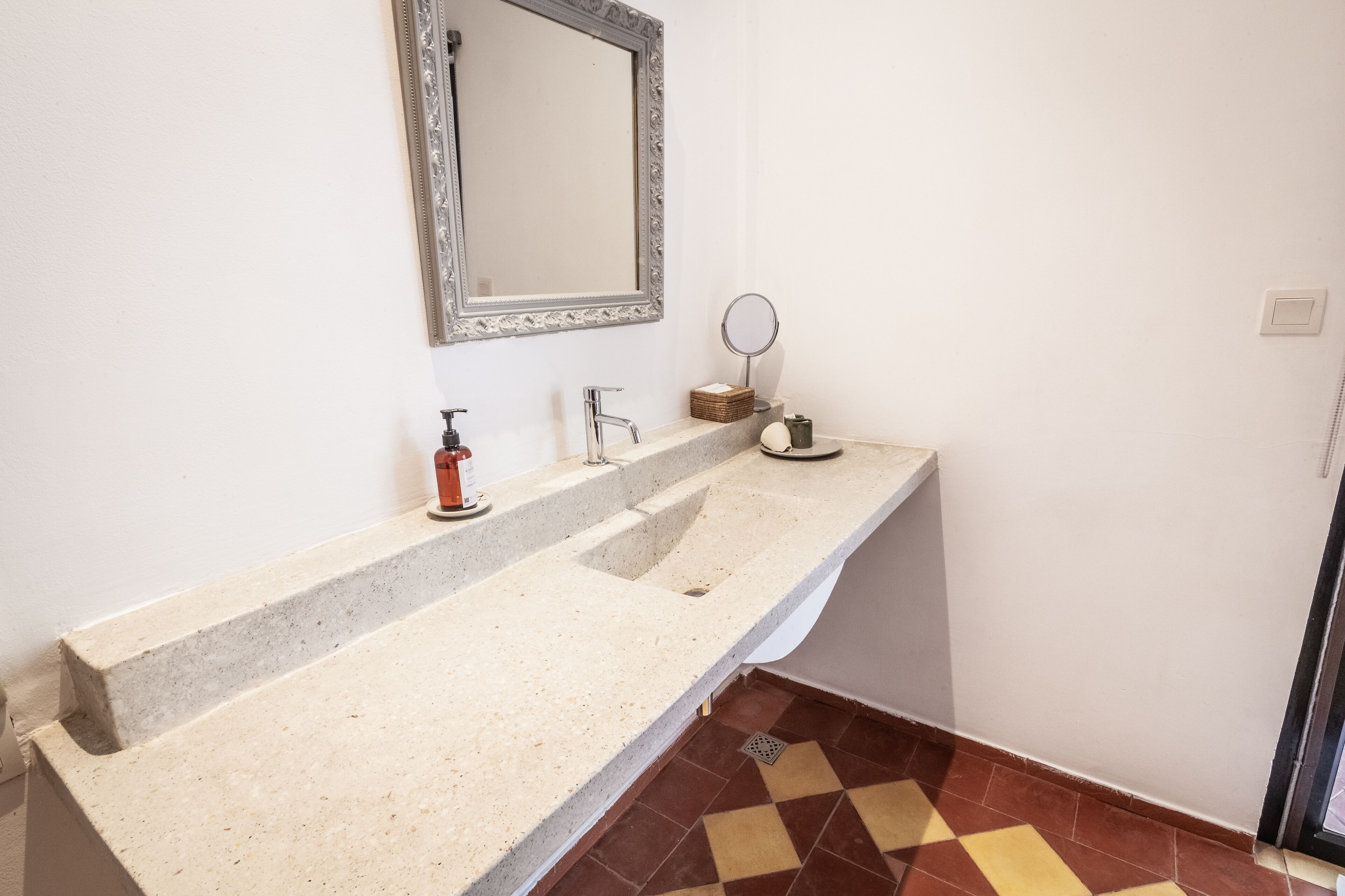 Un baño con encimera de granito, un lavabo, un espejo y un pequeño espejo redondo en la pared.