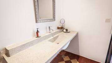 Un baño con encimera de granito, un lavabo, un espejo y un pequeño espejo redondo en la pared.