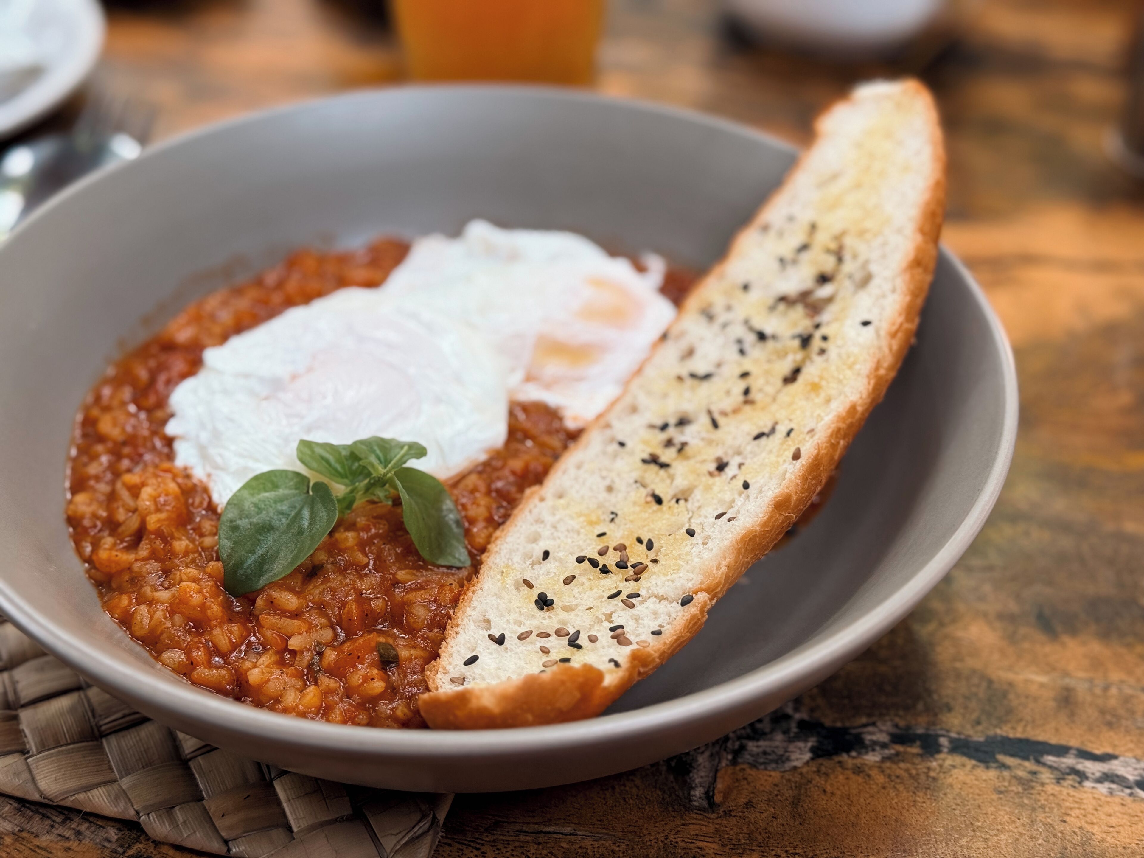 Un plato de estofado de lentejas con un huevo escalfado y una rebanada de pan adornada con semillas.