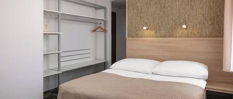 A hotel room with a bed, a wardrobe with shelves, a wooden headboard, and two wall-mounted lights.