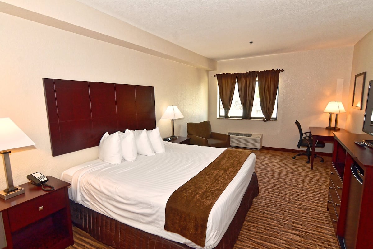 A hotel room with a large bed, bedside lamps, a desk with a chair, a television, and a window with curtains.