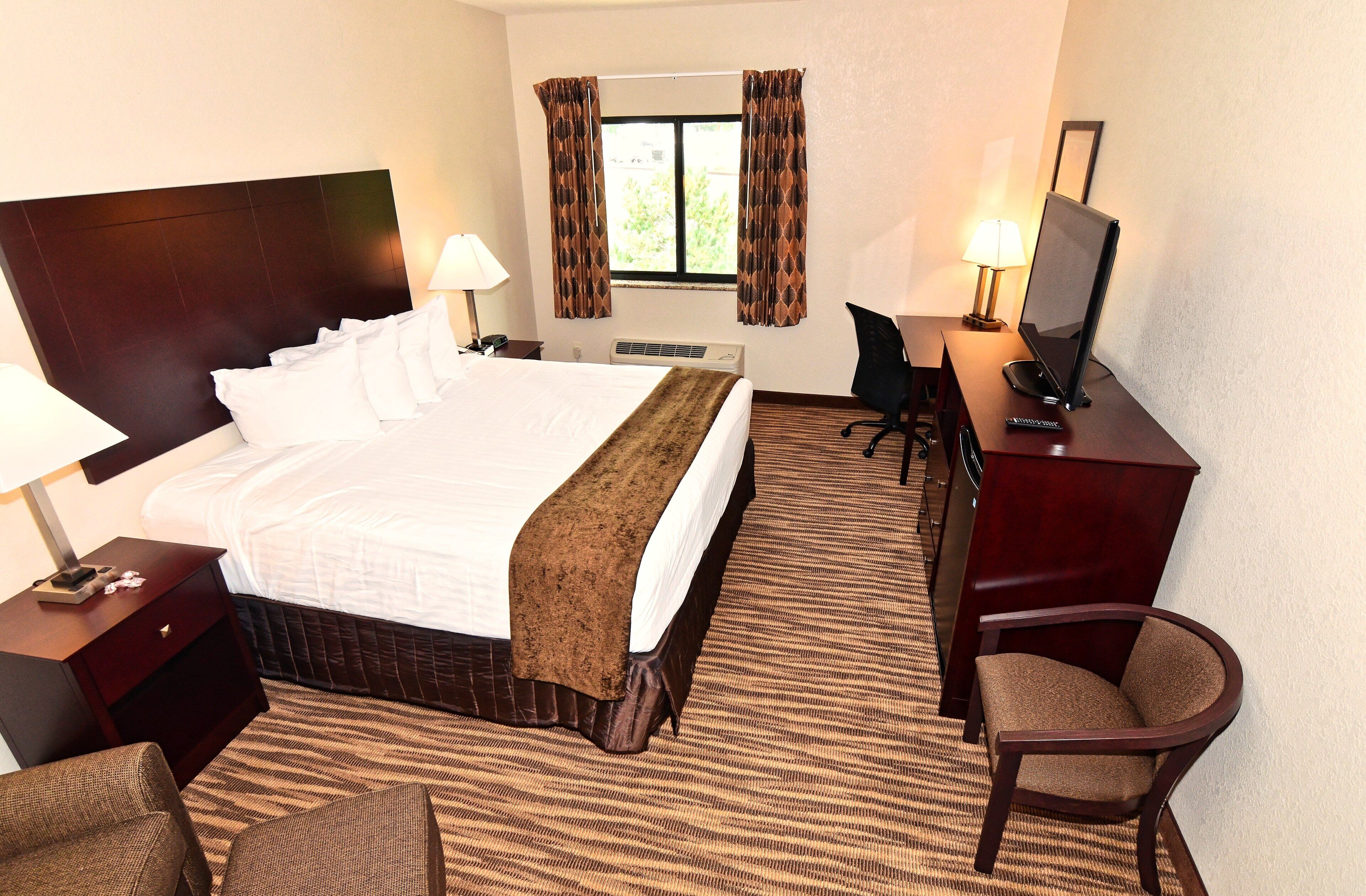 A hotel room with a large bed, a desk with a computer, a chair, and a window with curtains.