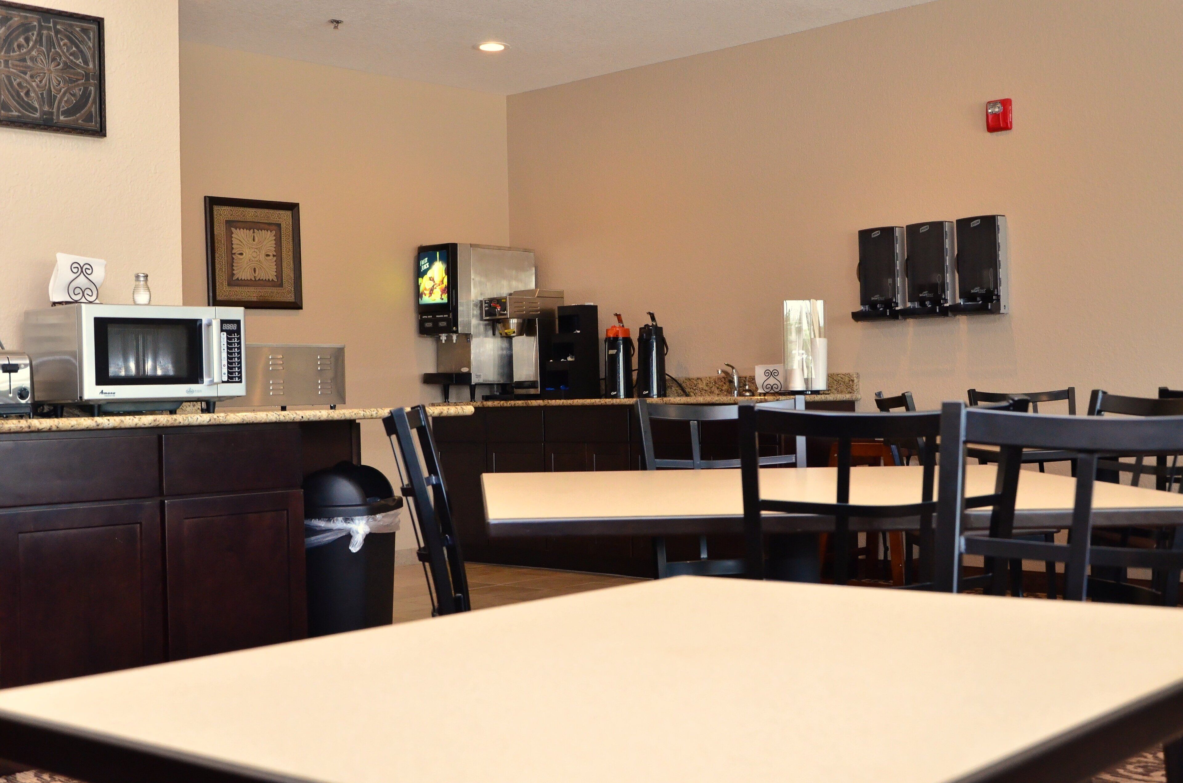 A dining area with tables and chairs, a microwave, a coffee machine, and a trash can.
