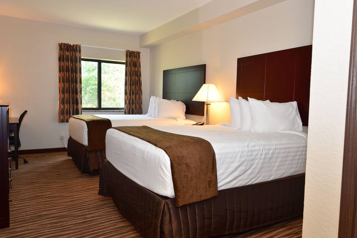 A hotel room with two beds, a desk, and a window with curtains.