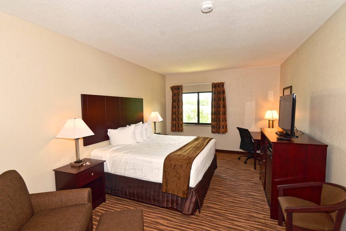 A hotel room with a large bed, two bedside tables with lamps, a desk with a chair, and a television.