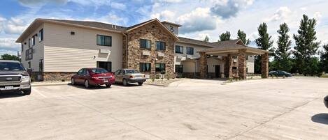 A multi-story building with a stone facade and a flat roof. There are several cars parked in front.