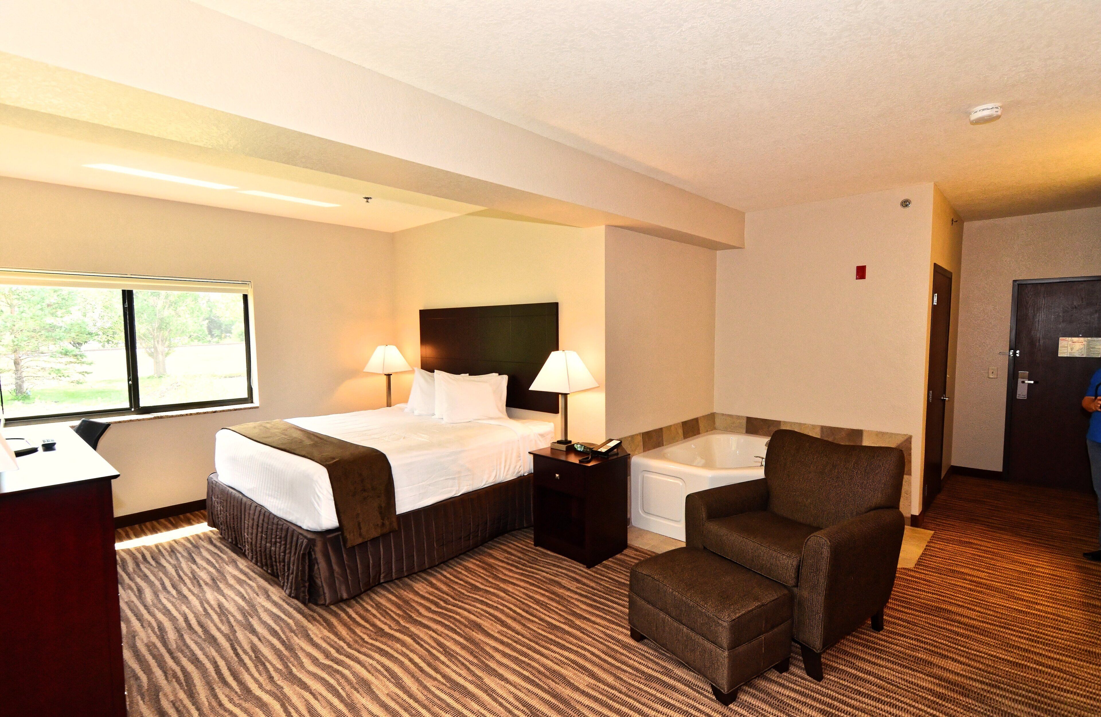 A hotel room with a bed, two bedside lamps, a chair, a desk, and a bathtub.