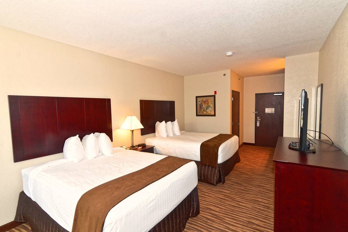 A hotel room with two beds, a desk with a TV, and a door leading to another room.