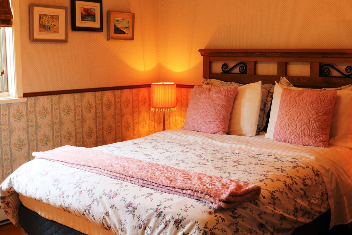 Ein ordentlich bezogenes Bett mit blumigem Bettzeug, ein Kopfteil mit dekorativem Design und eine Wandlampe.