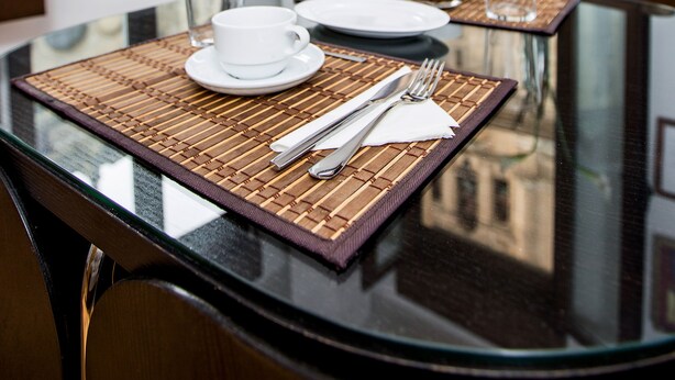 A dining table with a glass top, set with white plates, cups, and cutlery, and a clear glass. - Apartamentos Casa de la Lonja (Granada)