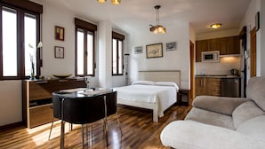 A modern bedroom with a bed, a sofa, a dining table, and a kitchen area. - Apartamentos Casa de la Lonja (Granada)